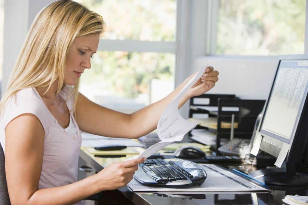 Mujer en su oficina de casa frente a un ordenador revisando unos papeles